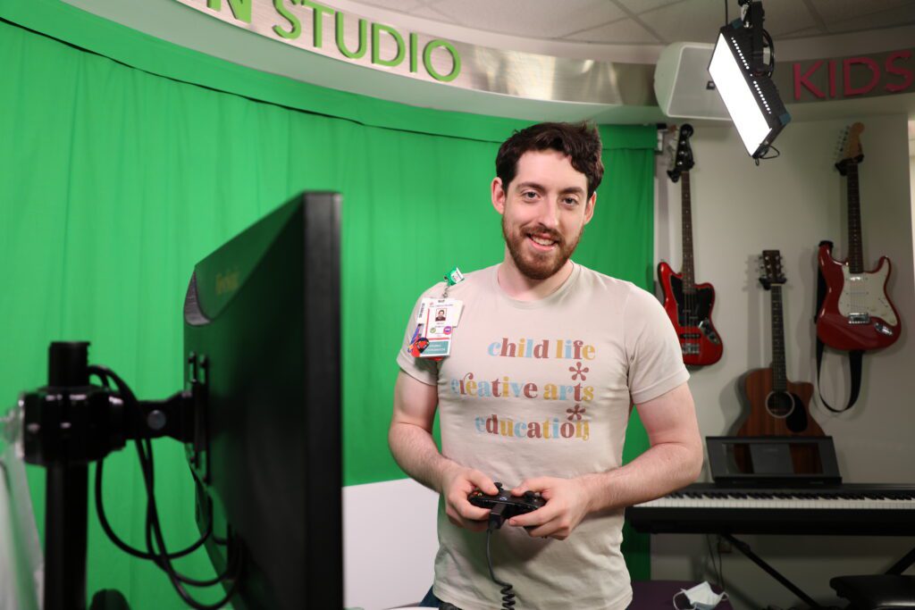 Texas Children's Patient Technology Coordinator holds a game controller in front of a green screen.
