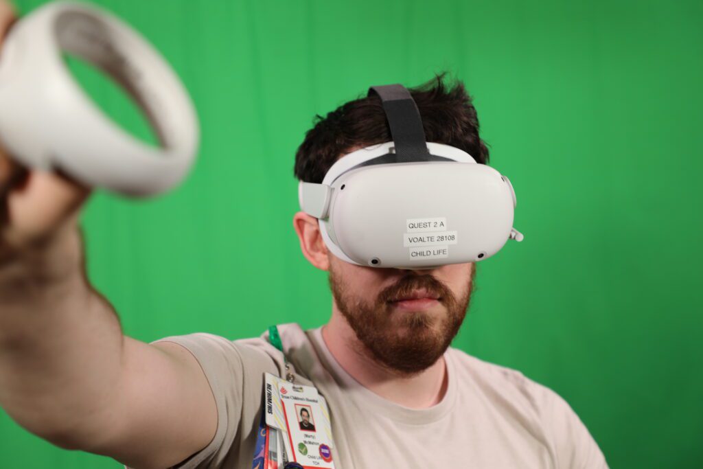 Patient Technology Coordinator Marty McMahon wears a VR headset in front of a green screen