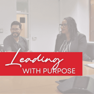 A healthcare leader sits at a conference table with her team members. Text reads "Leading with purpose."