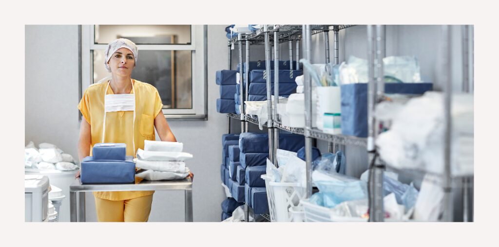 A nurse in yellow scrubs pushes a cart inside a medical supply closet.