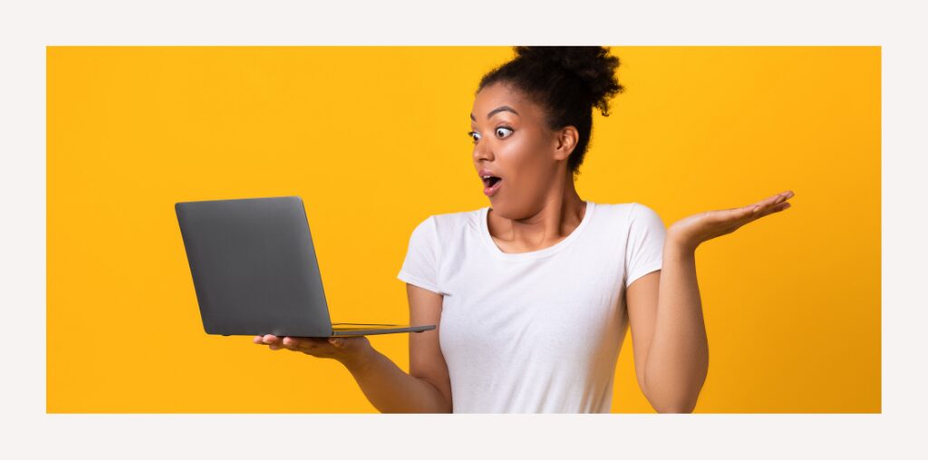 A woman in a white t-shirt appears surprised as she looks at the laptop she is holding.