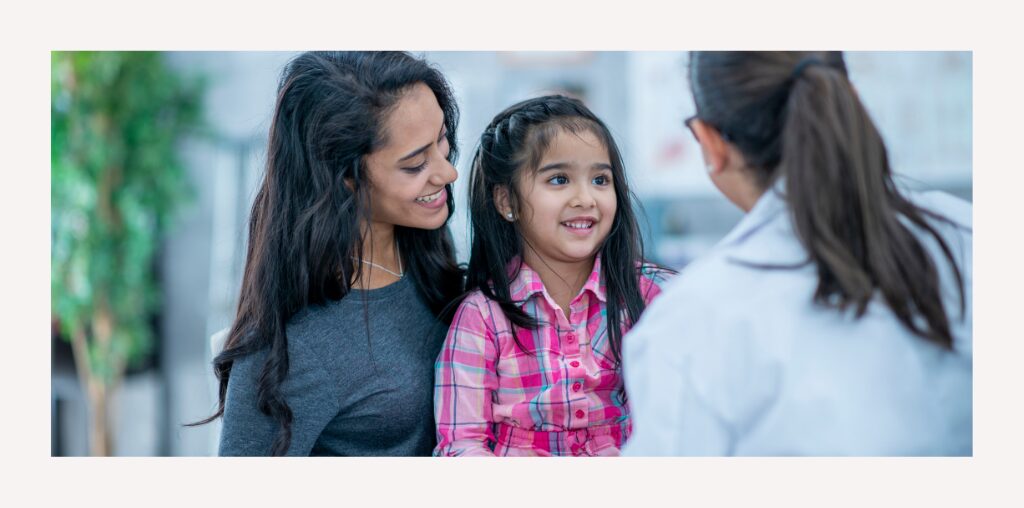 A little girl and her mother interacting with a medical professional with smiles on their faces.